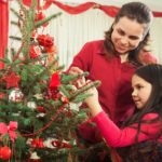 Image of mother and young daughter placing ornaments on Christmas tree, both dressed in bright red tops for happy holidays A.R.M. action resource management