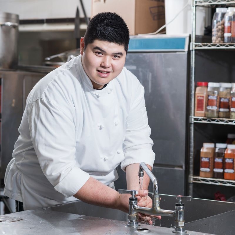 Image of happy chubby chef smiling as they wash their hands in kitchen food service safety ARM action resource management