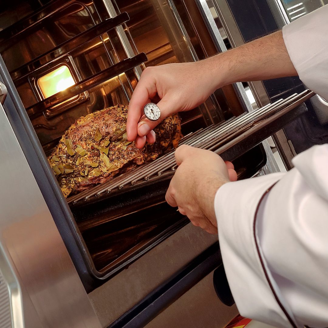 Image shows cook's hands checking a food thermometer in meat in an oven food service safety ARM action resource management
