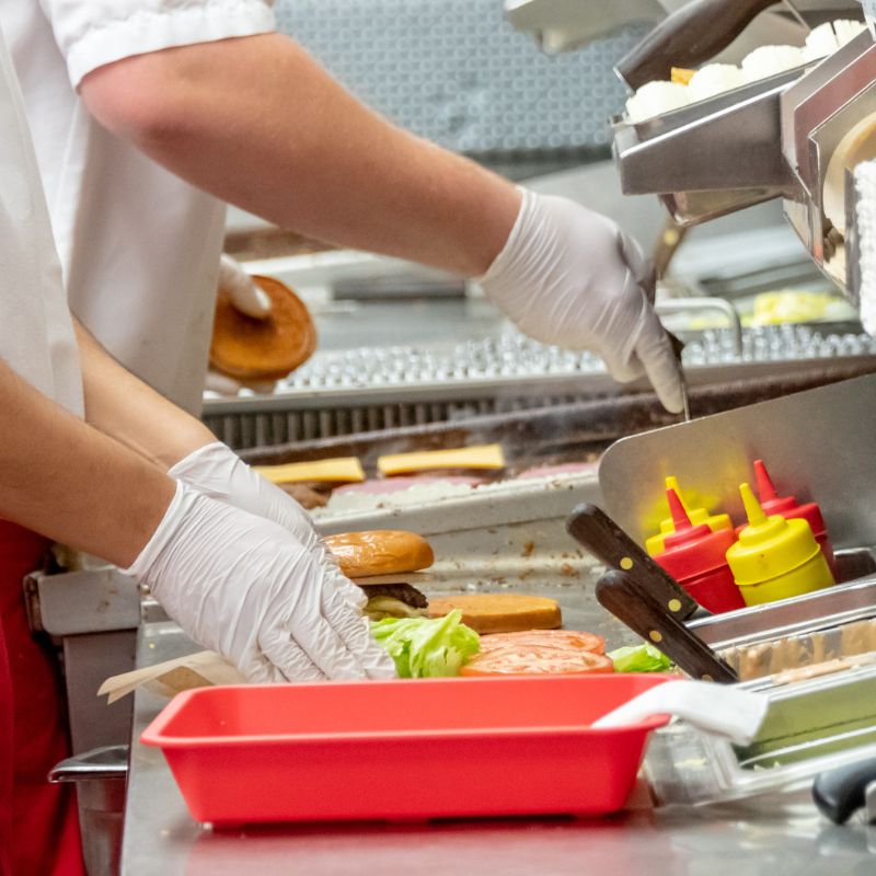 Image shows close-up of two food services workers' hands putting sandwiches together for food service safety ARM action resource management