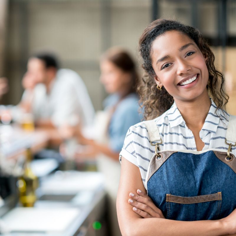Image of smiling food service worker with blurred restaurant guests behind for food service safety ARM action resource management