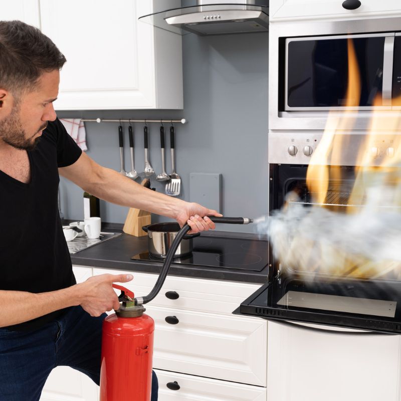 Image of young man using fire extinguisher to put out stove top fire in kitchen at home burn awareness ARM action resource management