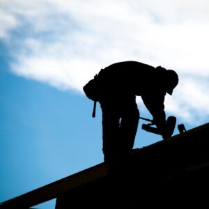 Image shows silhouette of worker bending over on roof to work with a blue sky and clouds behind for A.R.M. action resource management