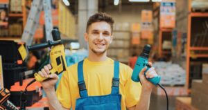 Image of happy young worker wearing blue overalls and holding a power drill in each hand tool safety A.R.M. action resource management