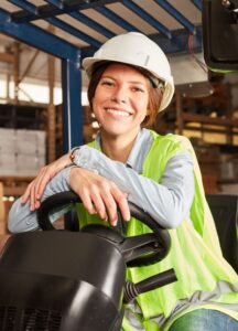 Image of smiling warehouse woman with yellow safety vest and white hardhat, seated on forklift A.R.M. action resource management