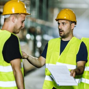 Image of two warehouse workers, both in yellow safety vests and hard hats, arguing or disagreeing conflict resolution A.R.M. action resource management