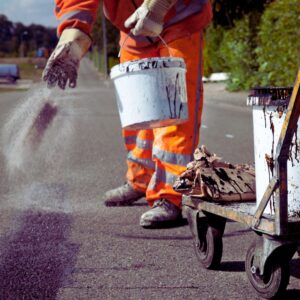 Image of road worker's gloved hands throwing an asphalt mixture onto the ground A.R.M. action resource management