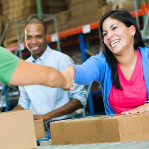 Image of smiling warehouse packers as one of them is reaching across a box shaking someone's hand A.R.M. action resource managment