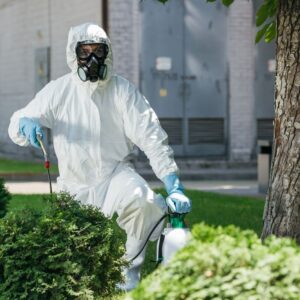 Image of gardener or landscaper wearing full white PPE suit with mask and gloves spraying chemicals outside. A.R.M. action resource management