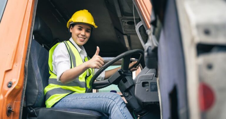 Image of a young woman truck driver wearing a yellow hard hat and yellow safety vest making "thumbs-up" and smiling from the truck cabin. Safety Tips for Delivery Truck Drivers A.R.M. action resource management
