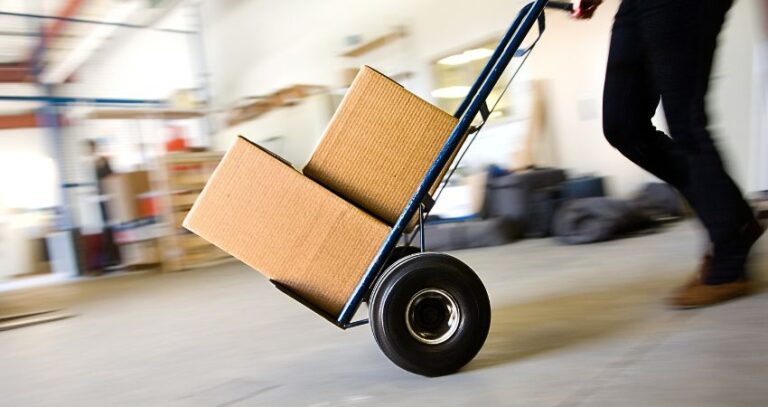 Image of warehouse worker (from the waist down) pushing a hand cart with two boxes. Hand Truck Safety. warehouse work. A.R.M. Action Resource Management