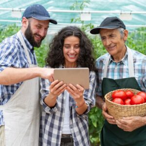 Image of a smiling woman greenhouse customer holding an iPad flanked by two male workers, both wearing checkered shirts and ball caps. One is holding a basket of tomatoes as they all look and smile at the iPad. Action Resource Management. A.R.M.