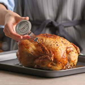 Image shows a home cook inserting a thermometer into a roasted chicken. For food safety. A.R.M. Action Resource Management.
