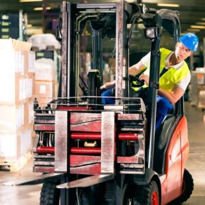 Image of a forklift driver wearing yellow safety vest and blue hard hat looking over to the left as he rounds a corner. A.R.M. Action Resource Management. safety training and services.