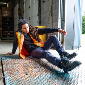 Image of a young warehouse worker wearing an orange and yellow safety vest on the dock floor after a slip, trip and fall. A.R.M. action resource management