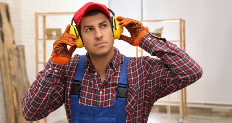 This image shows a handsome young worker, in blue overalls and a red/blue checkered shirt, red cap, gloves, and yellow PPE safety ear muffs. National Protect Your Hearing Month, October. Protect your hearing. A.R.M. Action Resource Management. Safety training.