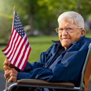 This image shows an American veteran of WWII, seated in a wheelchair with glasses and oxygen tubes, holding an American flag. A.R.M. Action Resource Management.