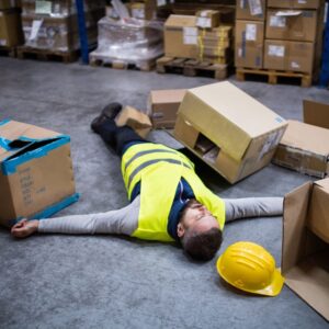 An image of a warehouse worker wearing a yellow vest, has fallen at work and is laying on his back, his yellow helmet on the floor nearby, with scattered boxes nearby. A.R.M. Action Resource Management Safety training, OSHA training