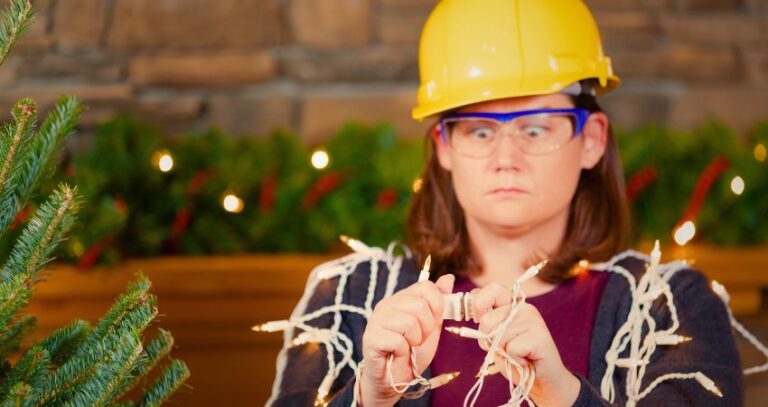 An image of a young person wearing a hard hat and safety goggles plugging two sets of holiday lights together while making an almost cross-eyed expression. Holiday safety tips A.R.M.
