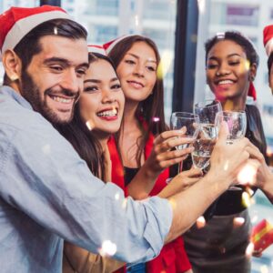 An image of young adults wearing Christmas hats, smiling, and cheering with their wine glasses. Holiday alcohol safety. A.R.M.