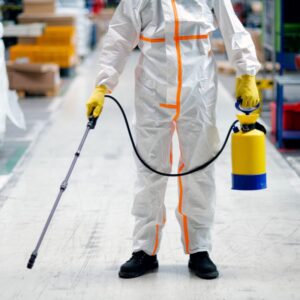An image of a worker fully clad in PPE and spraying a warehouse.