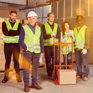 An image of five warehouse workers smiling at the camera, all wearing their PPE for safety first