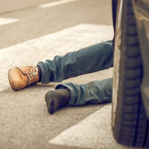An image of a person's legs on the street, in a sidewalk, with a car's tire behind it -- a distracted driver has hit a pedestrian.
