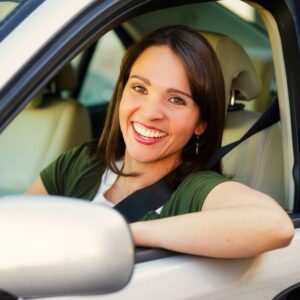 A young woman smiles at the photographer from the driver's seat of her car.