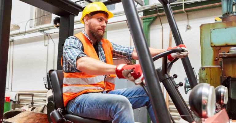 An image of a young forklift operator at work; wearing a hard hat, orange safety vest, and work gloves. Safety Tips for Forklift Operators