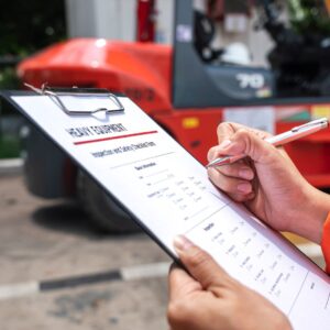 An image of a forklift operator's hands holding a clipboard in one hand with "HEAVY EQUIPMENT" written at the top, and a pen in the other hand, to conduct pre-operation checks. Safety Tips for Forklift Operators