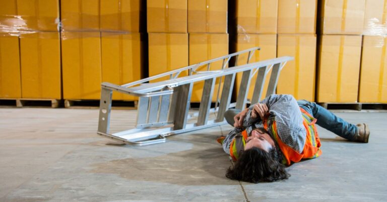 An image of a warehouse wounded on the ground, a ladder beside them. Slip and fall. Work injury. Warehouse hazards