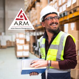 A smiling male warehouse worker wearing a hard hat, yellow safety vest, and safety glasses looking over his shoulder. The Action Resource Management A.R.M. logo is included.