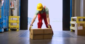 An image of a warehouse worker leaning down to pick up a box. Lifting Techniques