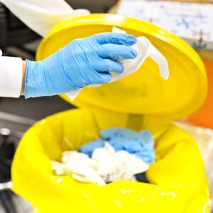 Close-up of a worker wearing gloves throwing toxic waste in a special bin.