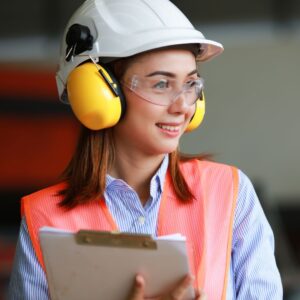 An image of a warehouse worker smiling as she wears PPE - Safety helmet, ear protection and eye guards.