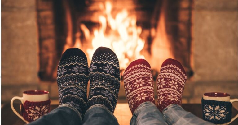 An image of two sets of winter sock-wearing feet in front of a roaring fireplace. Holiday Safety