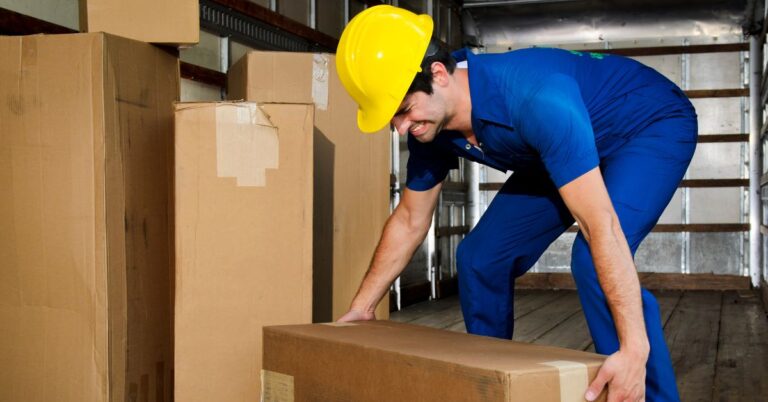 A warehouse worker grimaces as he tries to lift a box improperly.