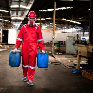 Image of a warehouse worker wearing all red PPE carrying two blue jugs with dangerous chemicals