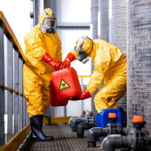 Two workers wearing yellow PPE suits and gas masks handling dangerous chemicals